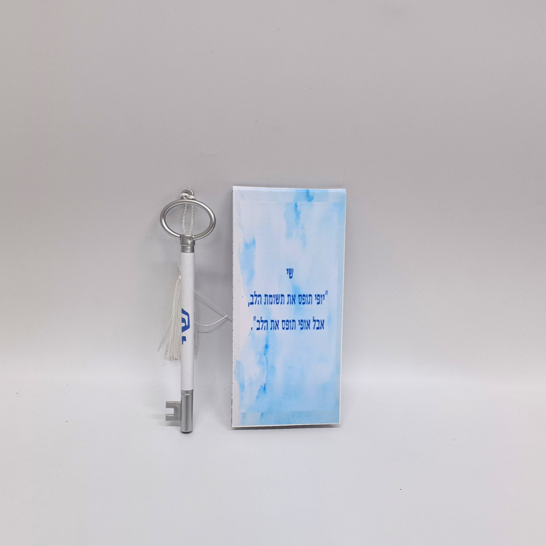 מפתח דקורטיבי לבן עם טאסל וכרטיס ברכה בעברית על רקע תכלת